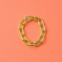 Load image into Gallery viewer, A gold chain link bracelet with a clasp closure, displayed on a solid coral pink background.